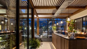 A modern interior with a wooden ceiling, glass walls, and a bar area with plants and bottles. - Magaggiari Hotel Resort (Cinisi)