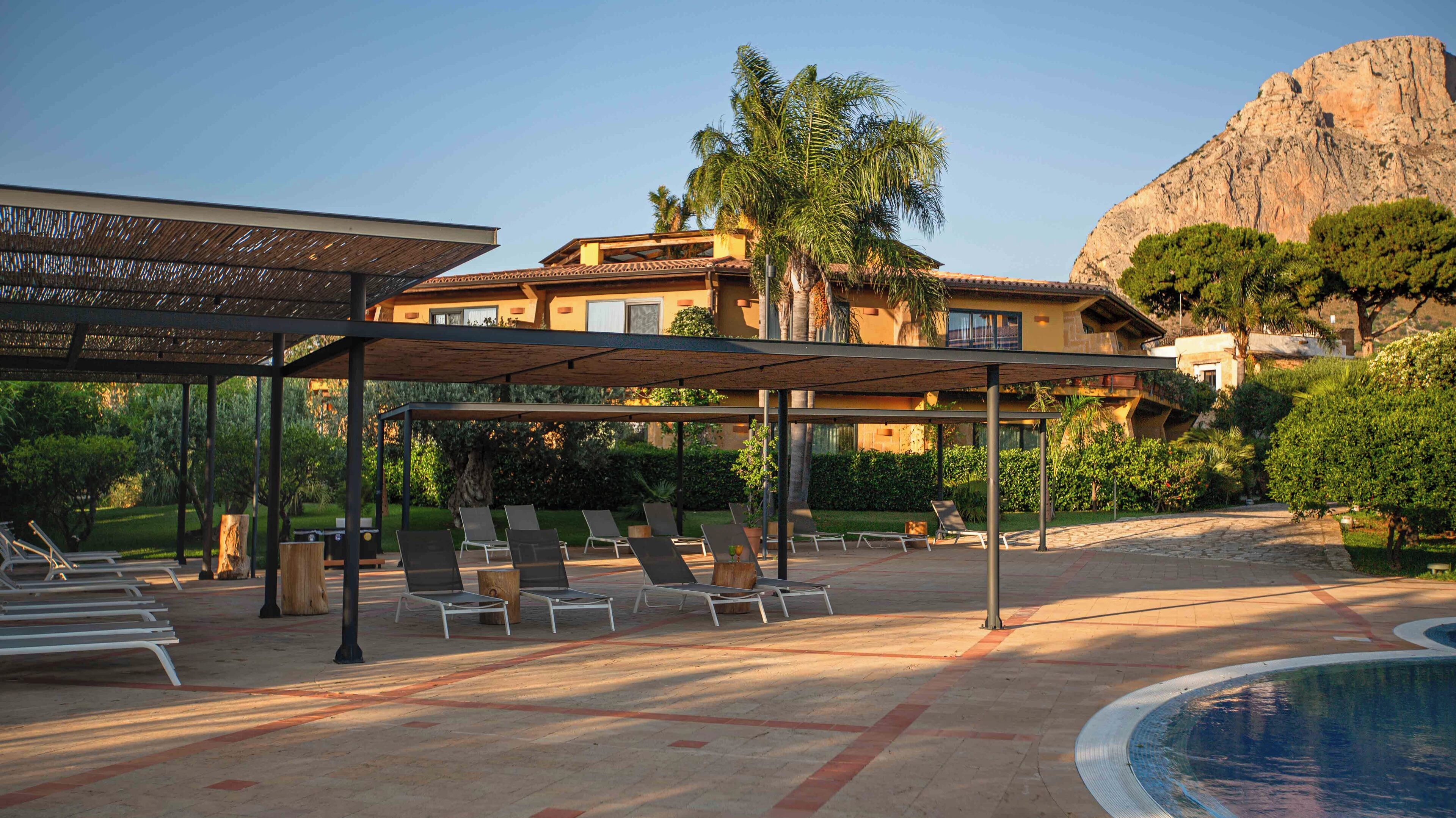 A resort with a pool, sun loungers, and a covered seating area.