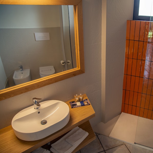 Un baño con lavamanos blanco, tocador de madera, espejo y zona de ducha con azulejos.