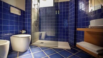 Une salle de bain avec des carreaux bleus, des toilettes blanches, un espace douche et un meuble-lavabo en bois doté d’un porte-serviettes.