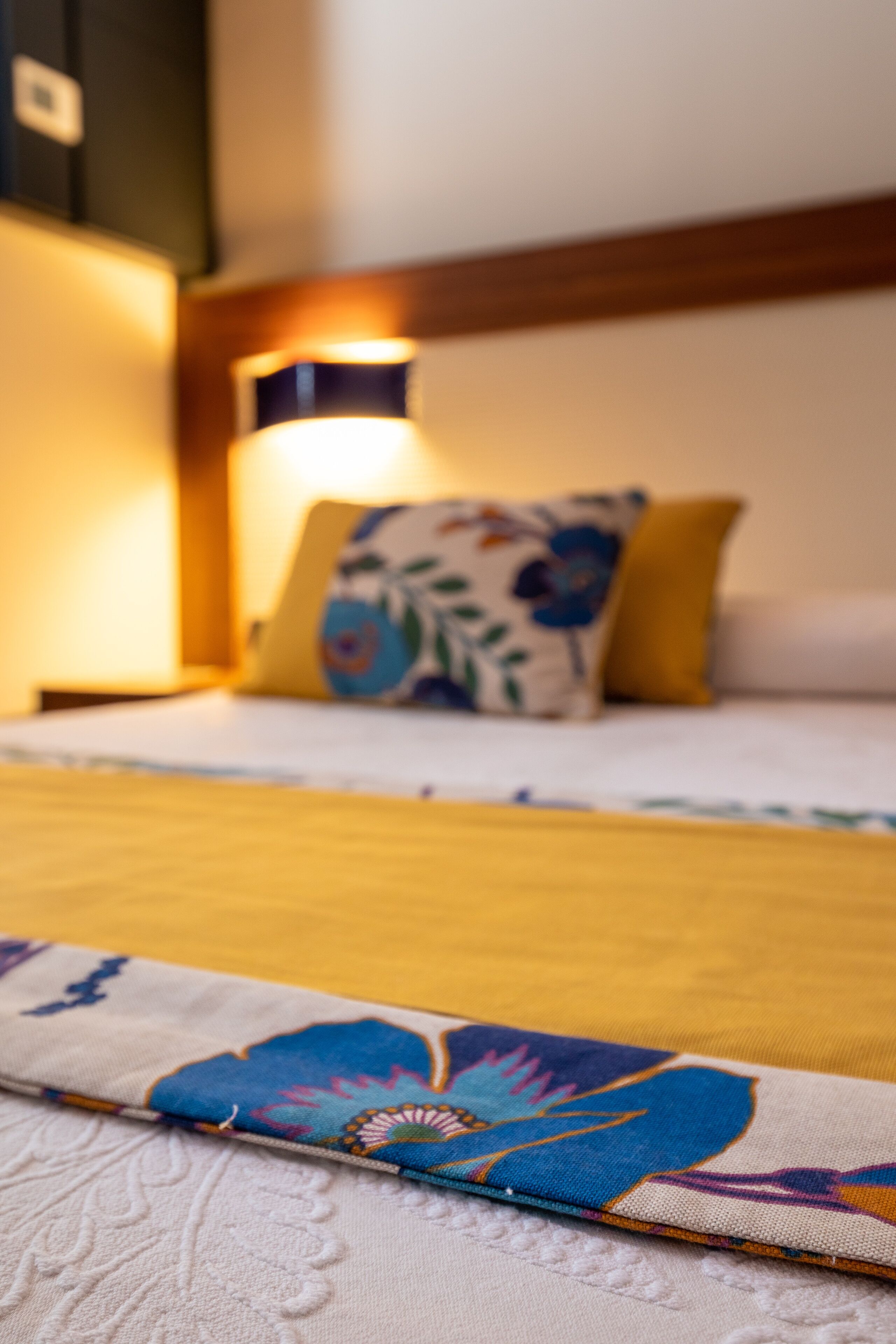 A bed with a floral bedspread and a yellow pillow.