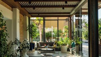 A modern indoor space with a wooden ceiling, large windows, and potted plants.