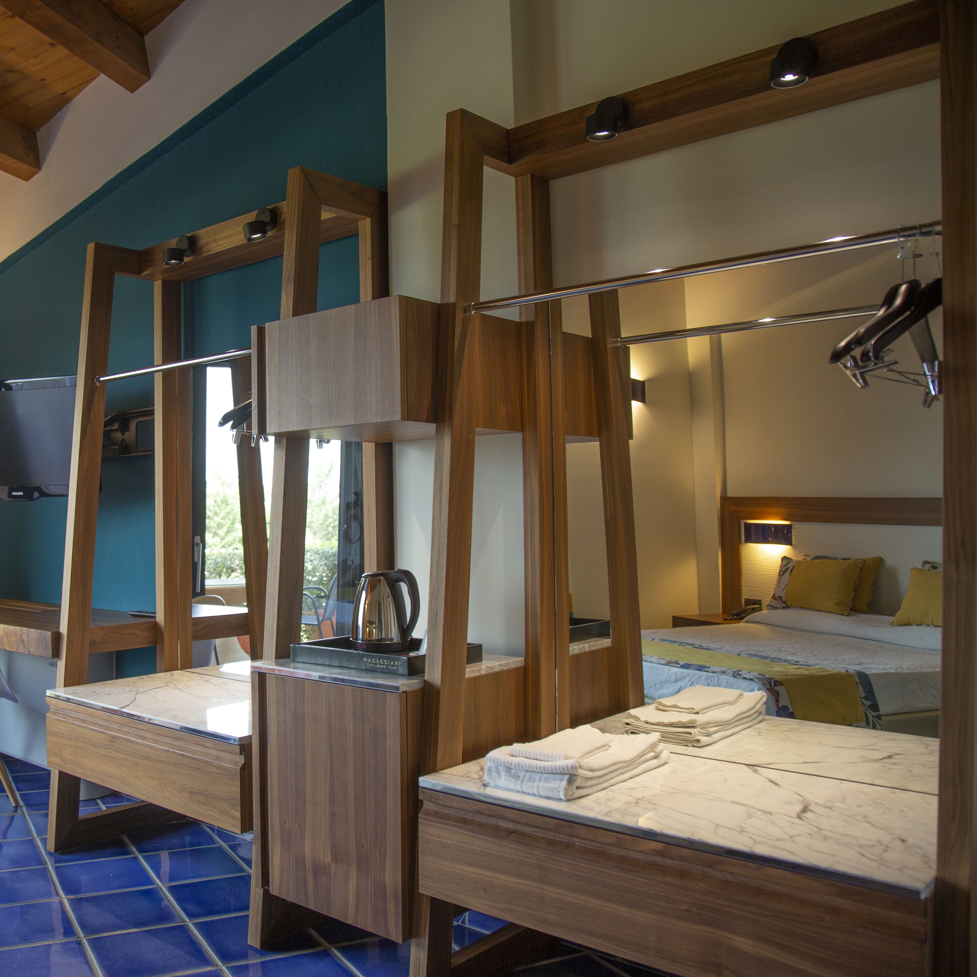 Ein Hotelzimmer mit einem Bettgestell aus Holz, einem eingebauten Schreibtisch mit Wasserkocher und einem großen Spiegel.