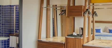 Habitación de hotel con estructura de cama de madera, una silla de madera, una mesita y un baño visible a través de una puerta abierta.