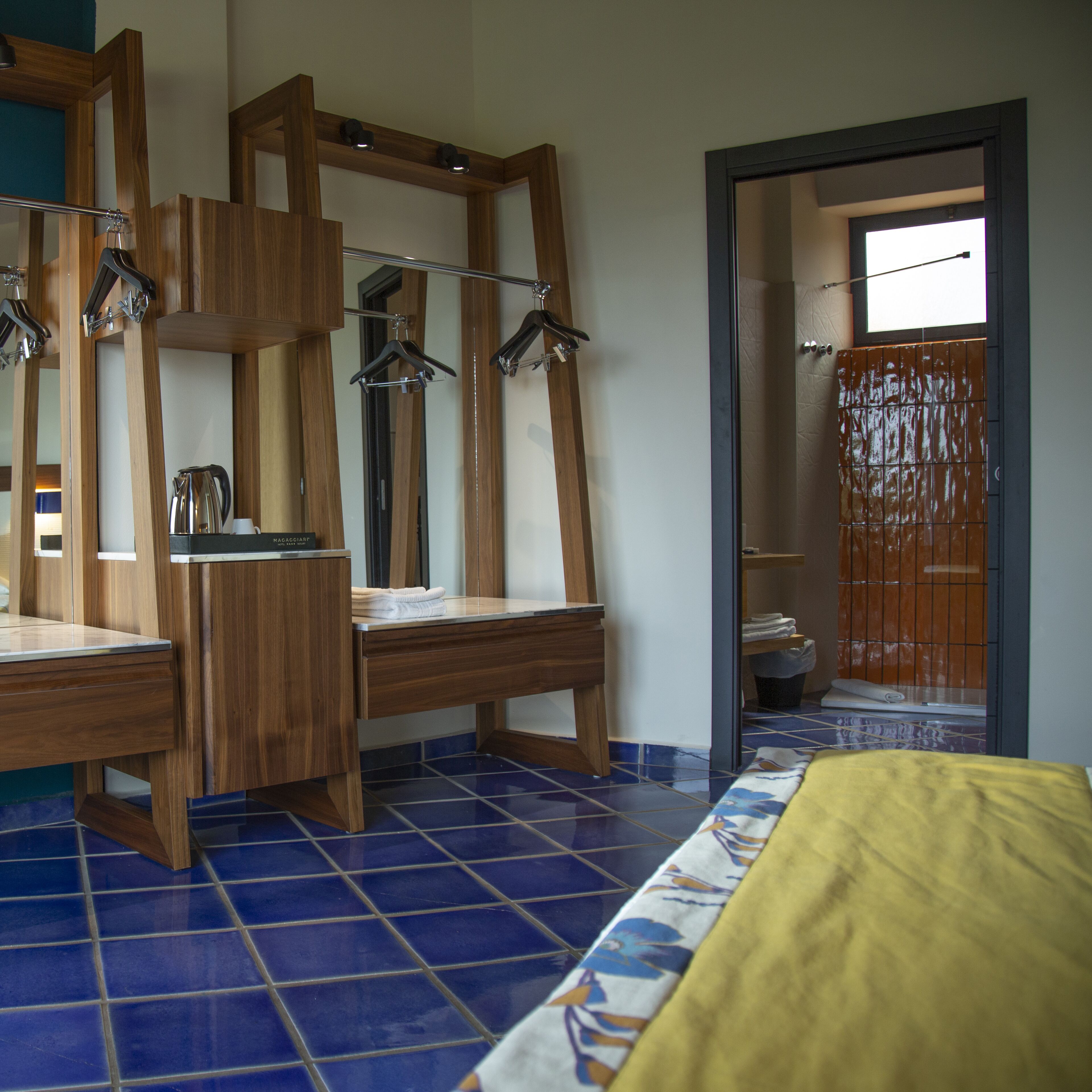 Habitación de hotel con escritorio de madera, cama con cubrecama amarillo y baño con ducha y piso con baldosas.