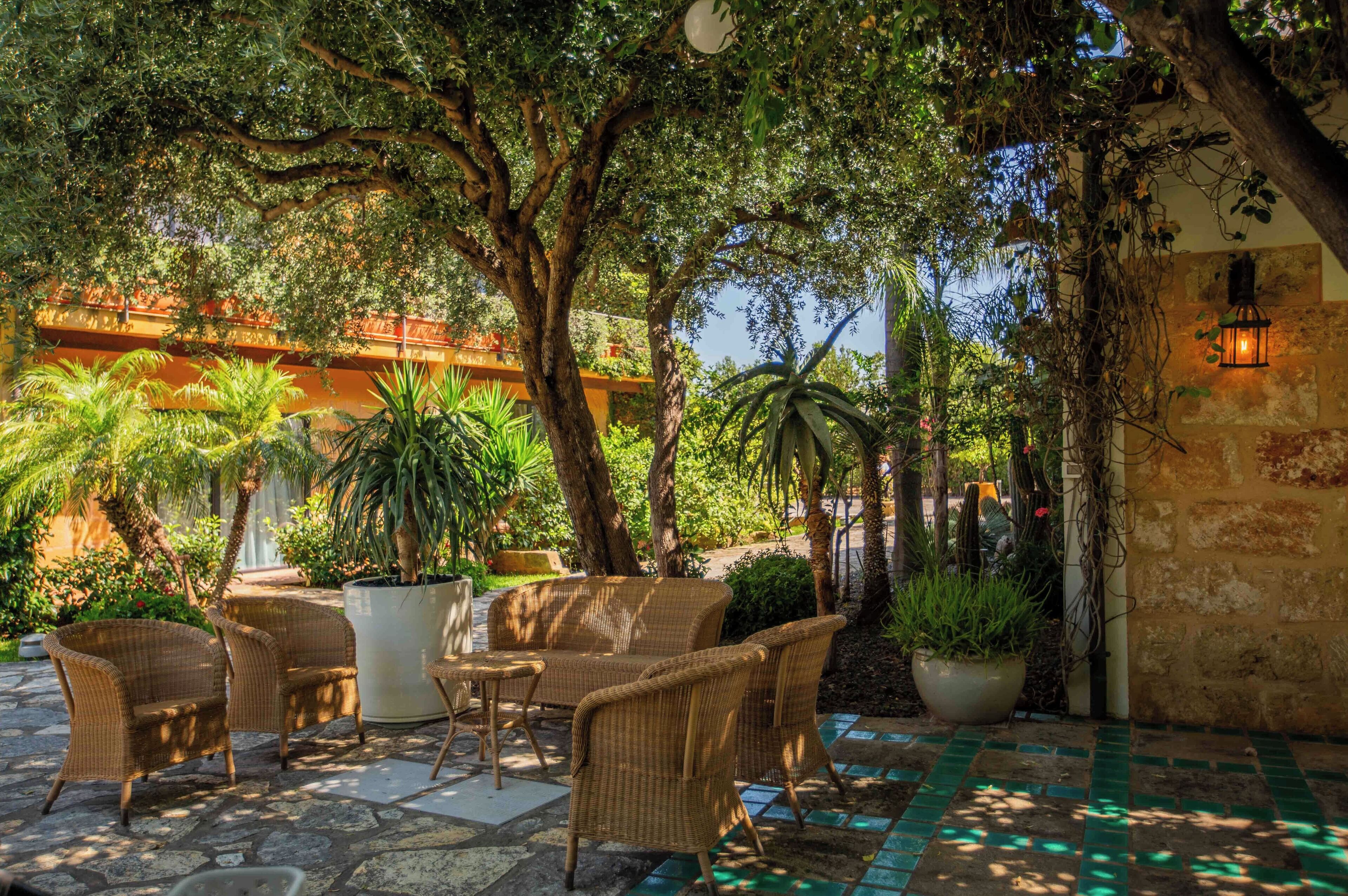 An outdoor patio with wicker furniture, potted plants, and a stone-tiled floor.