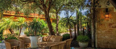 An outdoor patio with wicker furniture, potted plants, and a stone-tiled floor.