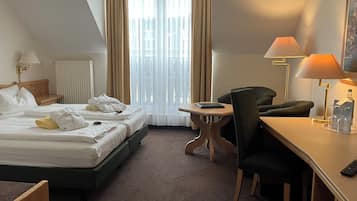 Habitación de hotel con cama, escritorio, silla, lámpara y ventana con cortinas.