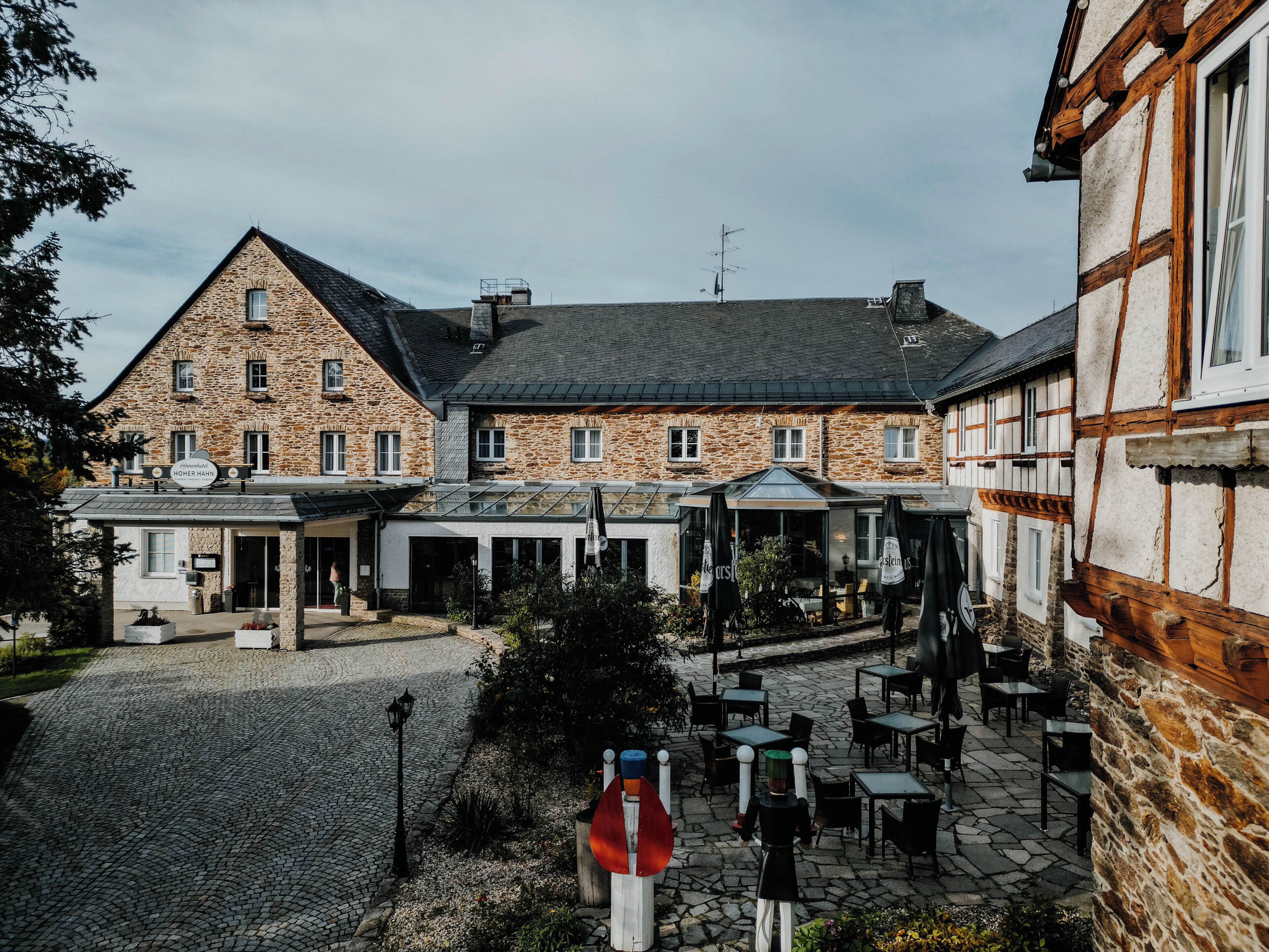 A traditional stone building with a courtyard featuring outdoor seating and a sign reading "Hohen Hain".