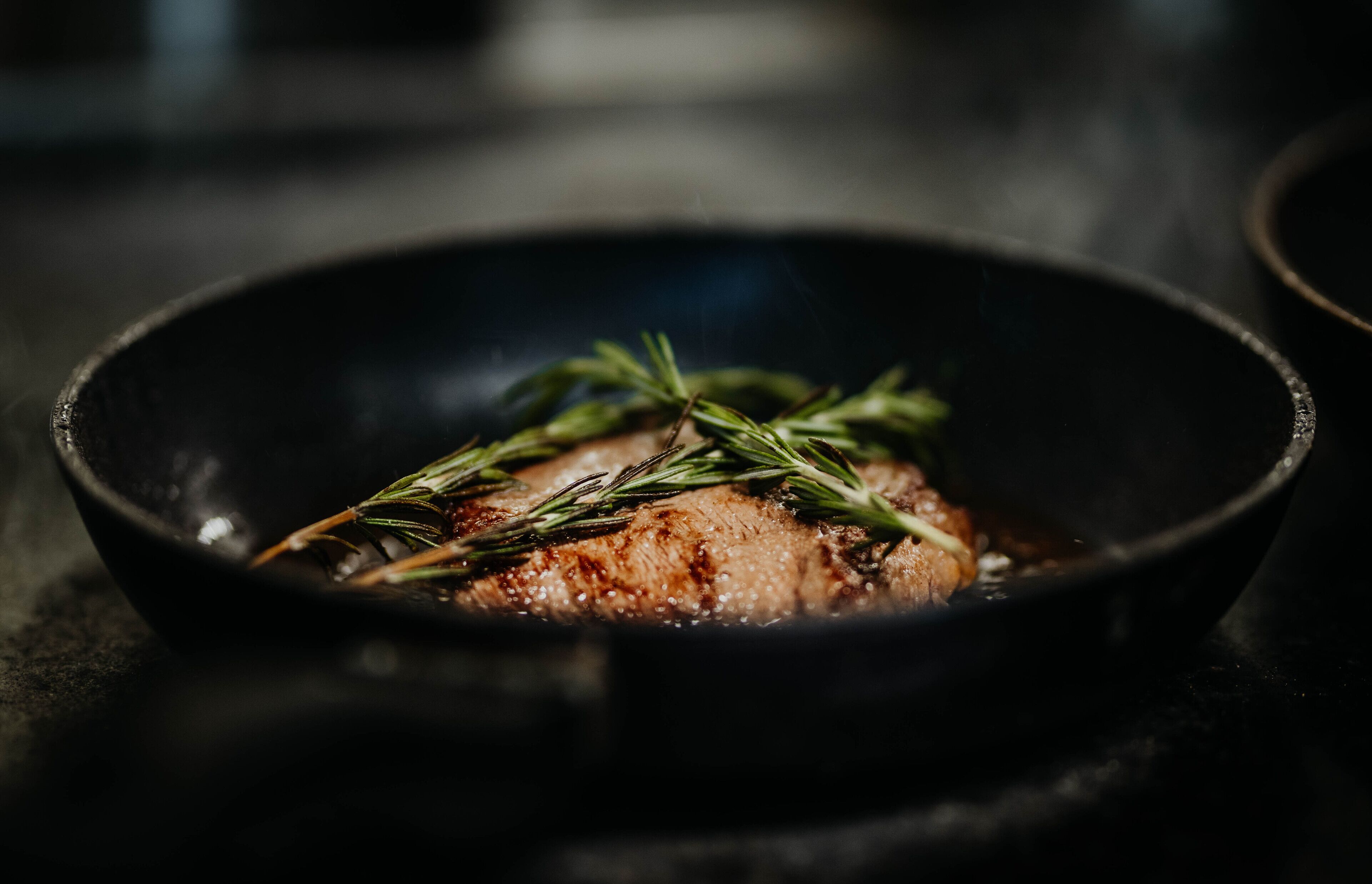 A pan with a cooked steak and rosemary.