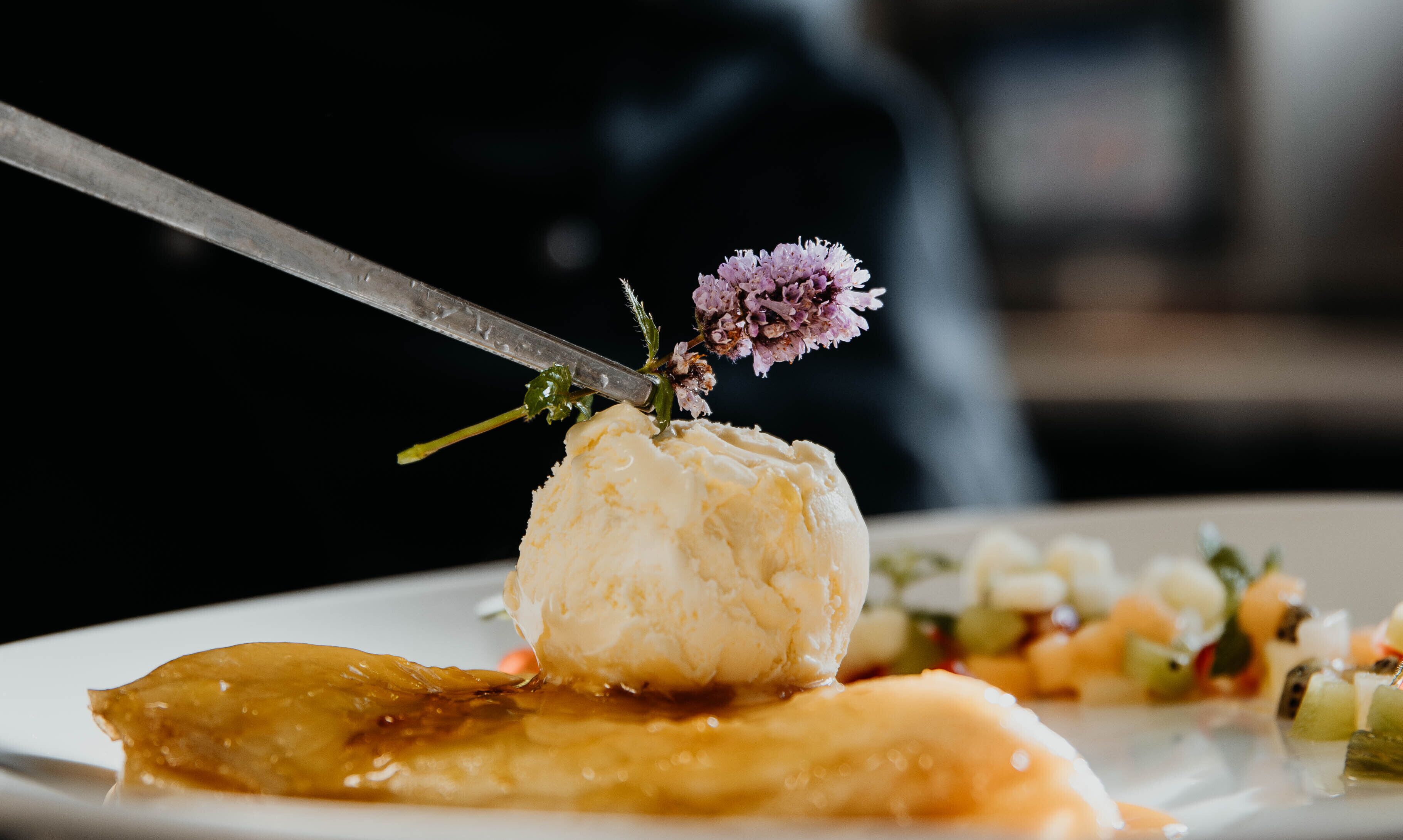 A dessert with a scoop of ice cream on a plate, garnished with a flower and a knife.