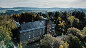 A large building with multiple windows and a chimney, surrounded by trees and hills in the background. - Sonnenhotel Hoher Hahn (Schwarzenberg/Erzgeb.)