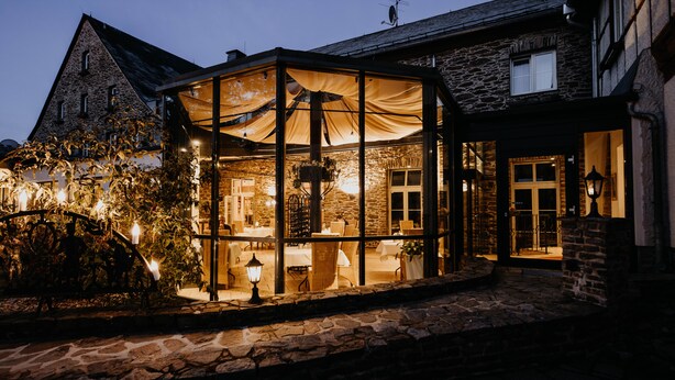 A stone building with a glass-enclosed dining area, stone steps, and outdoor lighting. - Sonnenhotel Hoher Hahn (Schwarzenberg/Erzgeb.)
