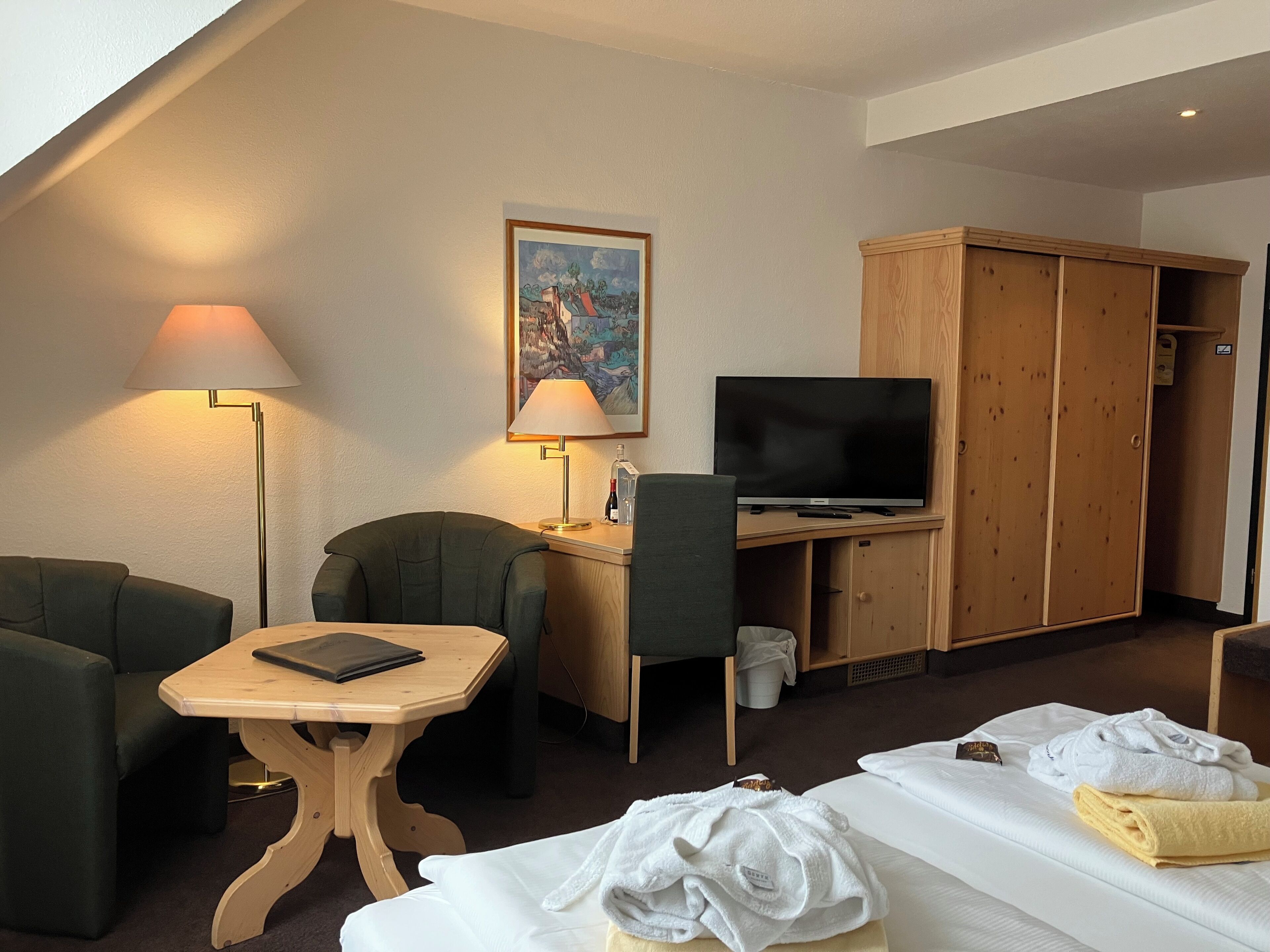 Ein Hotelzimmer mit Bett, Schreibtisch mit Fernseher, Stuhl, Lampe und Kleiderschrank.