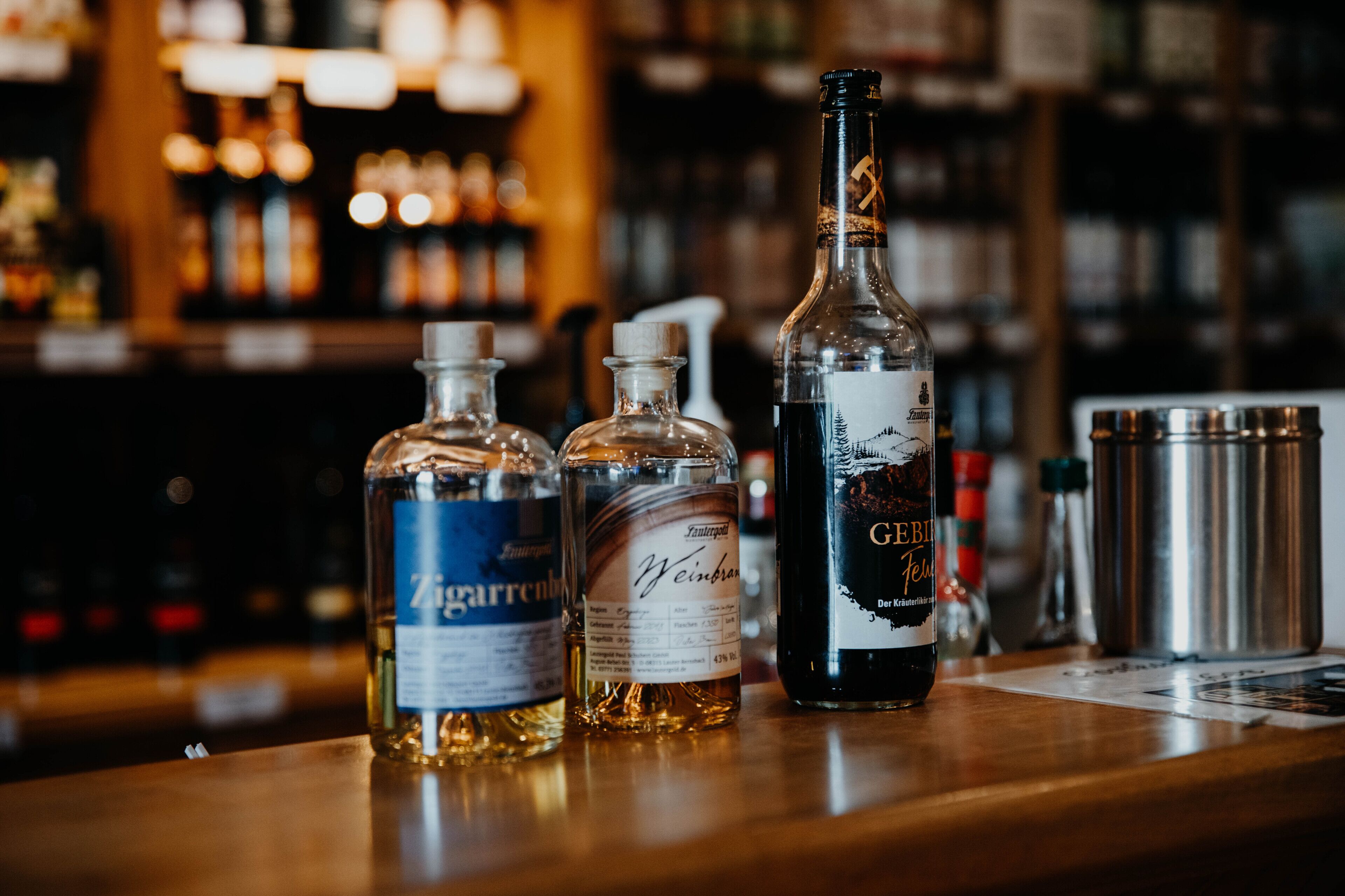 Drei Alkoholflaschen auf einer Bar, im Hintergrund unscharf sichtbare Regale.