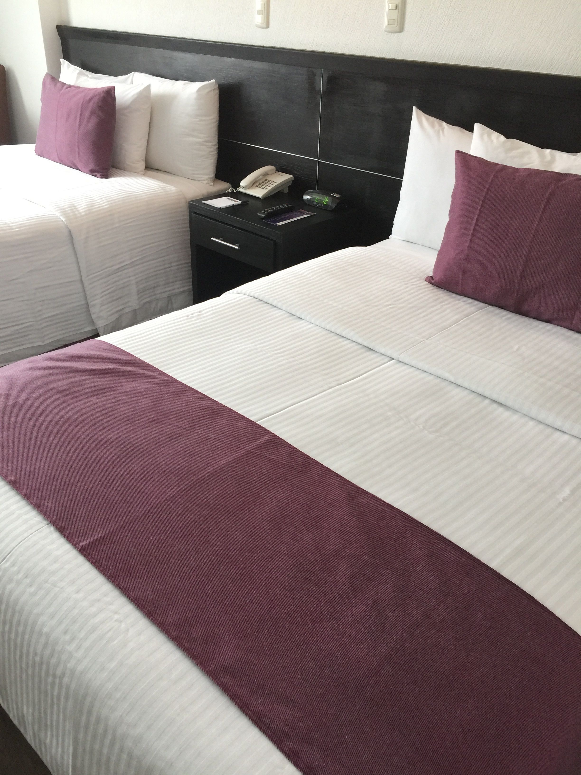 A hotel room with a large bed, a bedside table with a phone, and a nightstand with a clock.