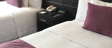 A hotel room with a large bed, a bedside table with a phone, and a nightstand with a clock.