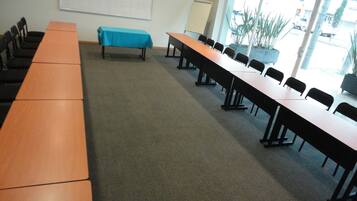 A conference room with long tables and chairs, a projector screen, and a view of the street through large windows.