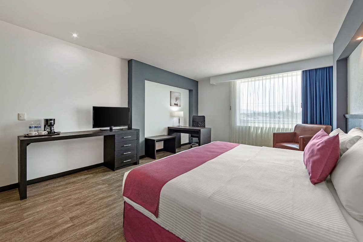 A hotel room with a bed, a desk, a chair, a television, and a window with curtains.