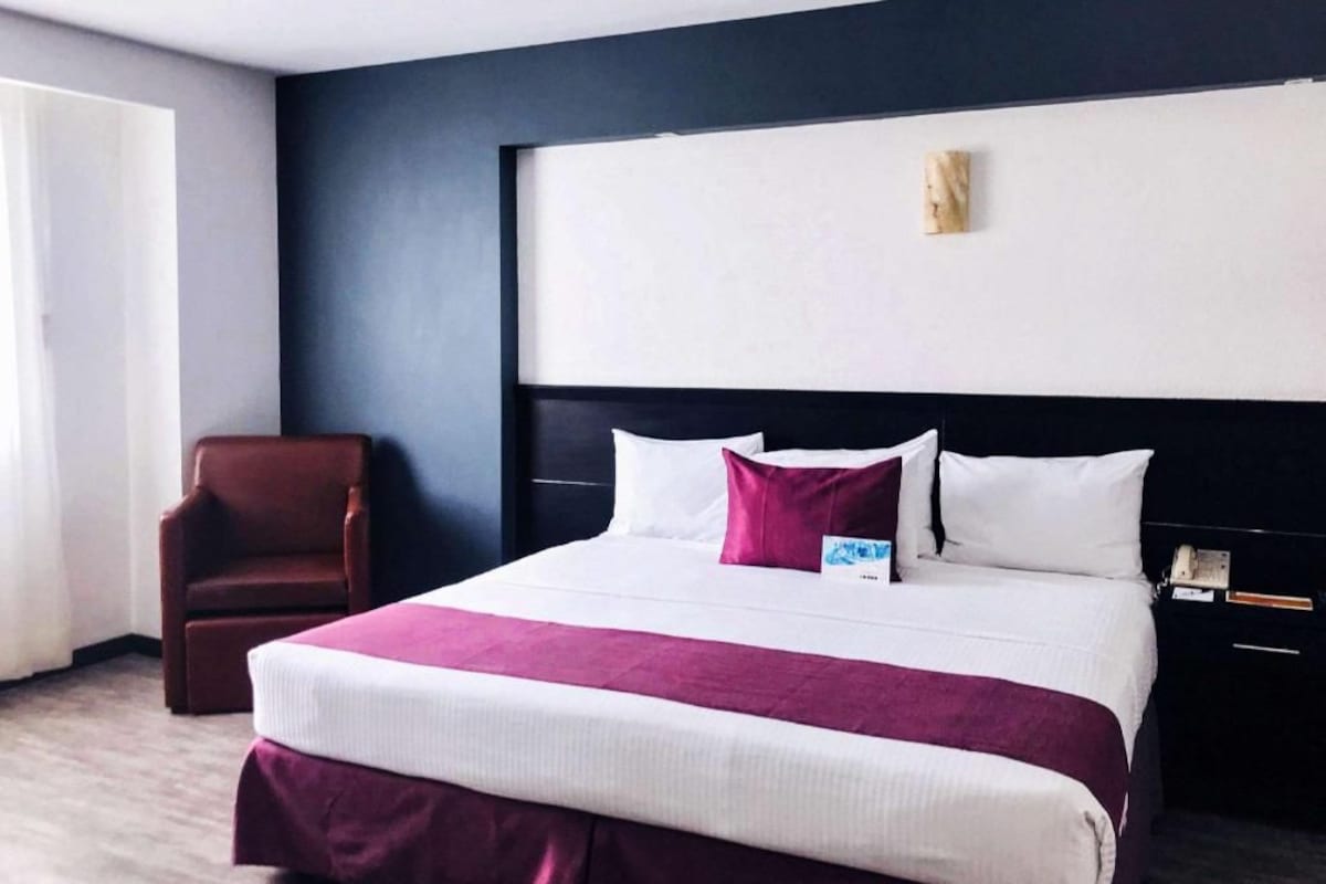 Una habitación de hotel con una cama grande, una silla, una mesita de noche y una obra de arte colgada en la pared.
