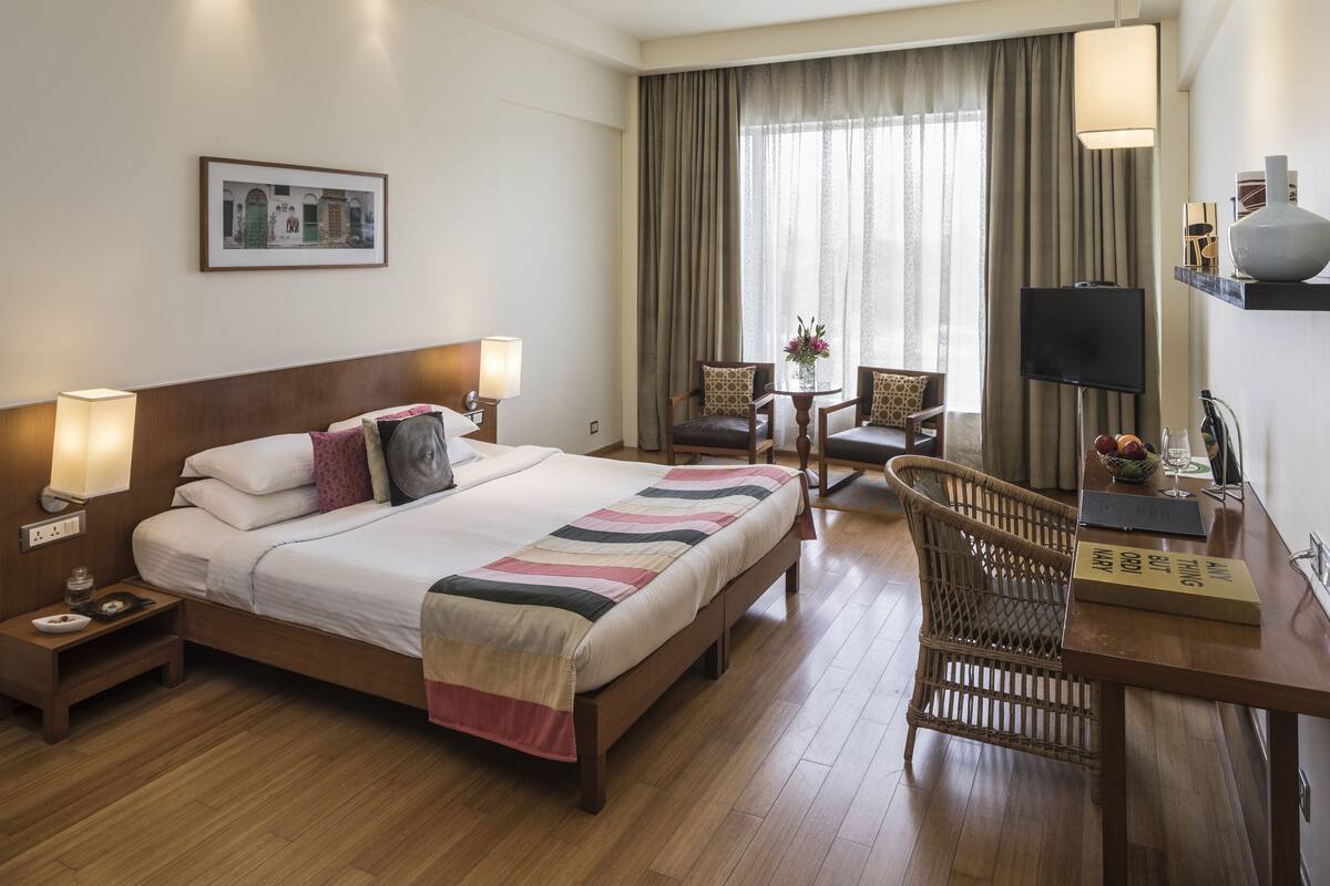 A hotel room with a large bed, bedside tables, a desk with a chair, a television, and a window with curtains.