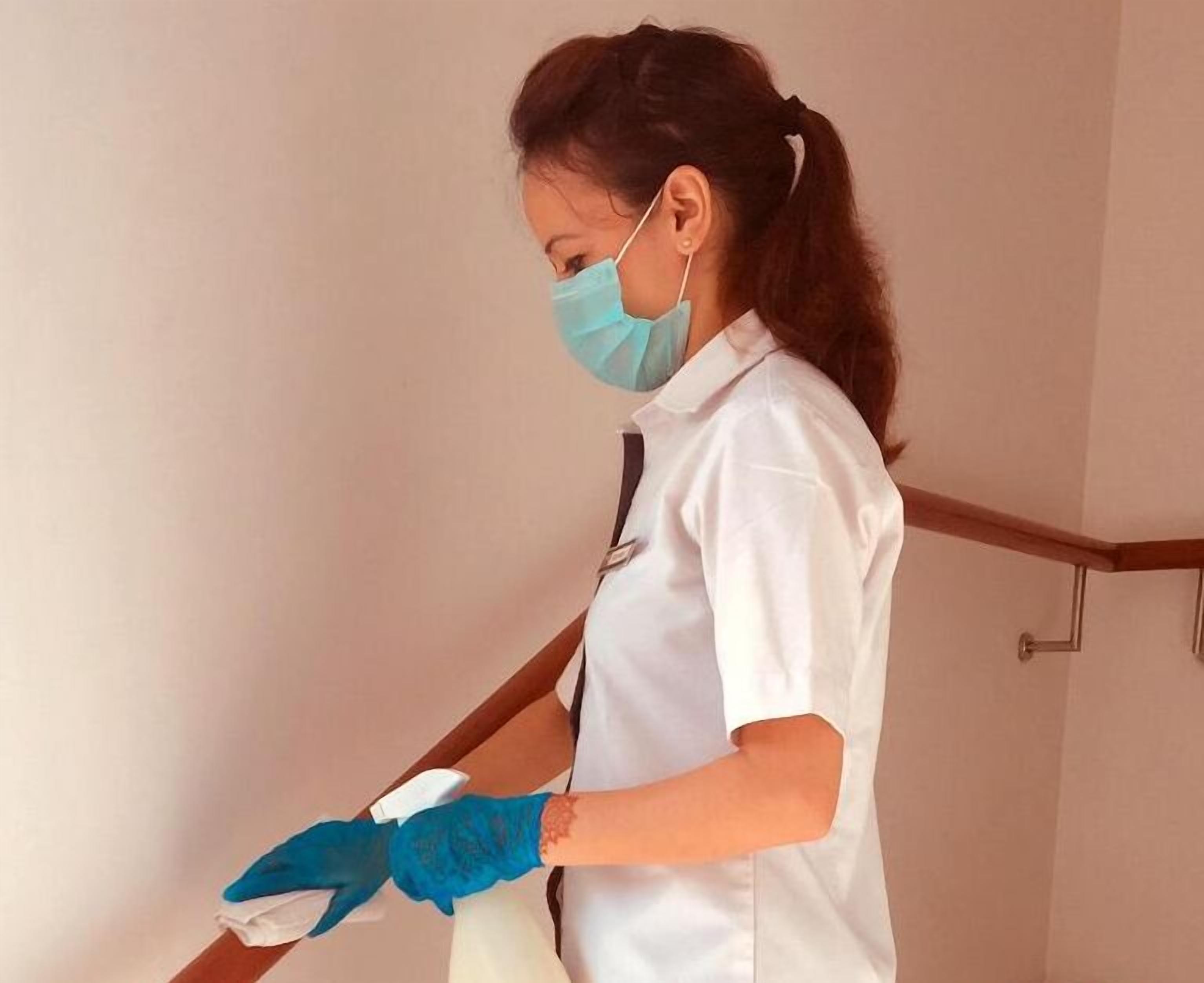 Una persona con uniforme blanco y guantes azules limpiando un piso de madera.
