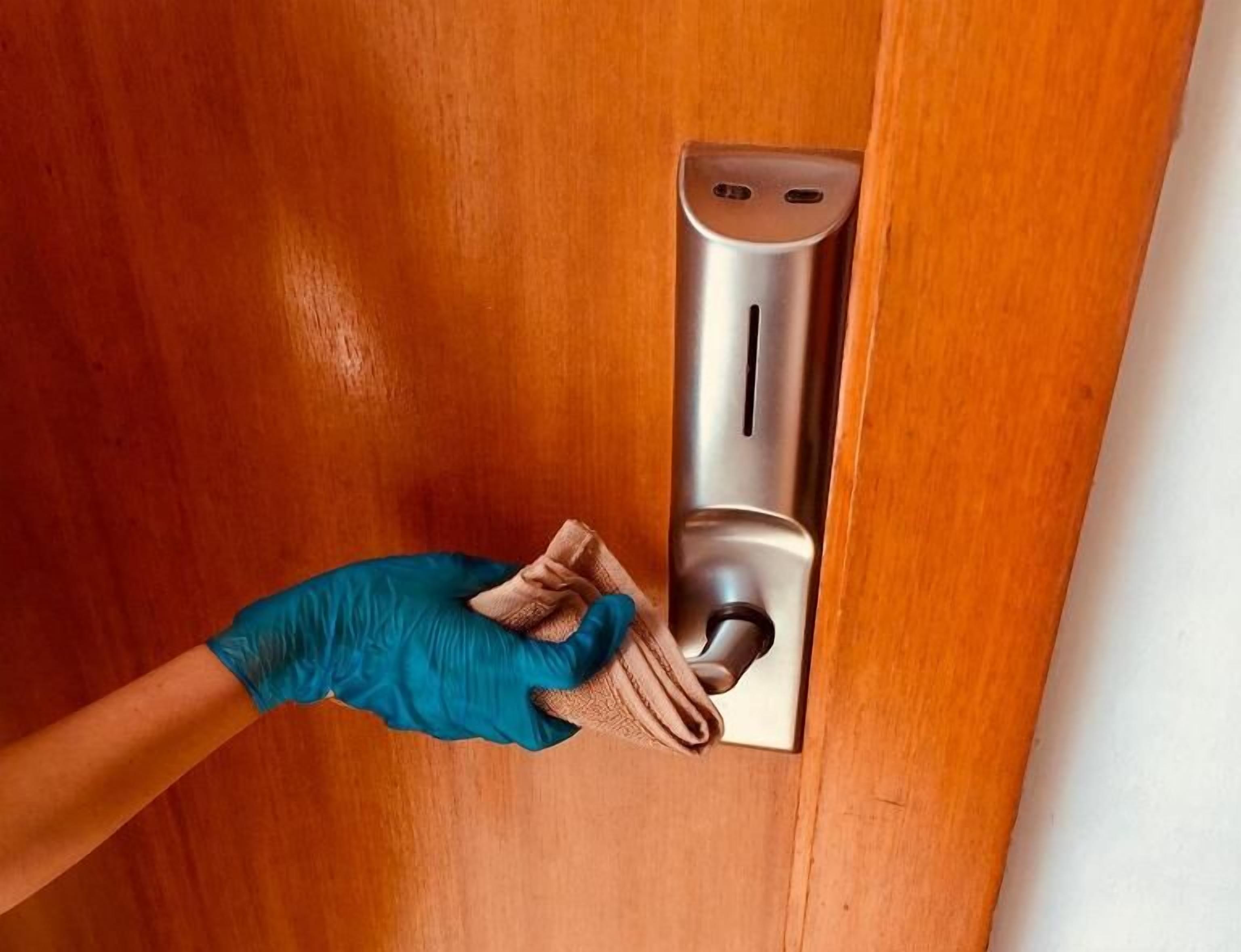 Une personne nettoie une poignée de porte métallique avec un chiffon.