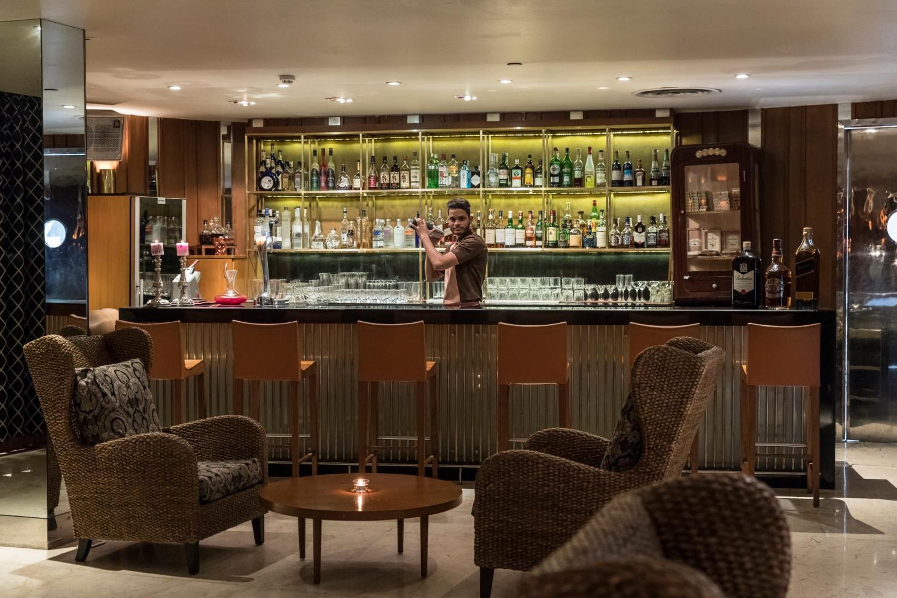 A bar area with wicker chairs, a bar counter with various bottles, and a well-lit interior.