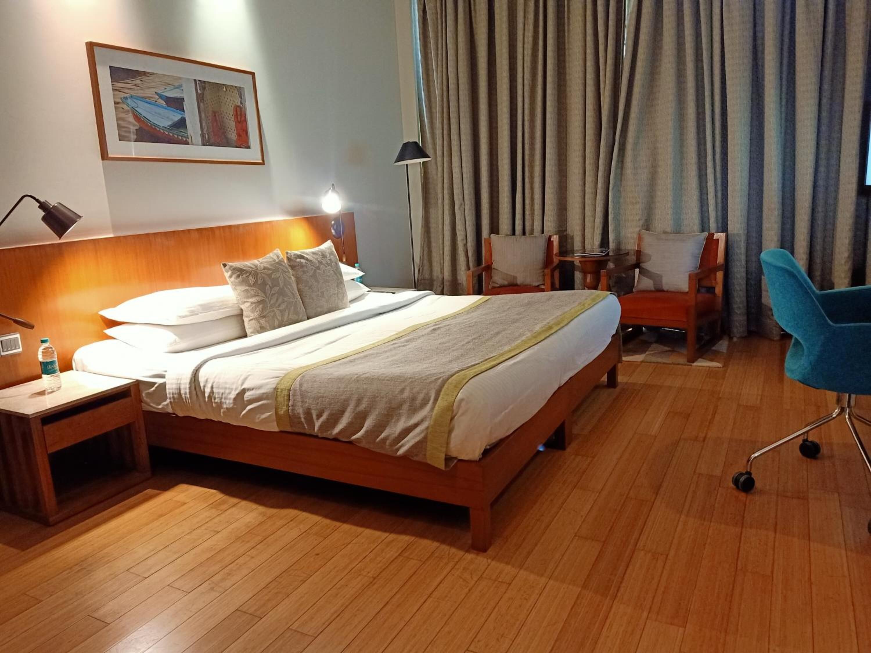 Una habitación de hotel con una cama de madera, una mesita de noche, una silla, un escritorio y una lámpara.