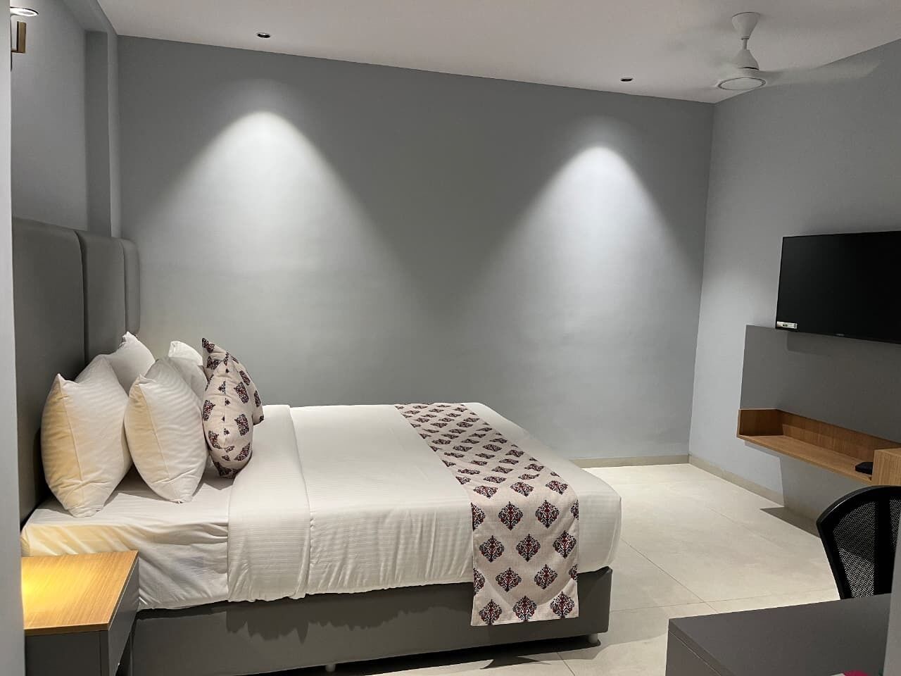A modern bedroom with a bed, pillows, a bedside table, a TV, and a ceiling fan.