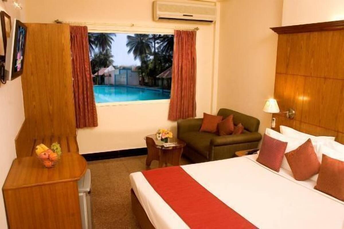 Habitación de hotel con cama, escritorio, silla, mesita, sofá y ventana con cortinas.