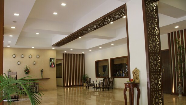 A spacious lobby with a polished floor, a reception desk, seating area, decorative panels, and wall clocks. - Ramanashree California Resort (Bengaluru)