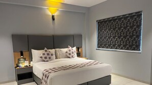 A modern bedroom with a large bed, bedside tables, a wall-mounted light, and a patterned window blind. - Ramanashree California Resort (Bengaluru)