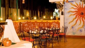 An outdoor dining area with tables and chairs, a white structure, and a mural with a sun design. - Ramanashree California Resort (Bengaluru)
