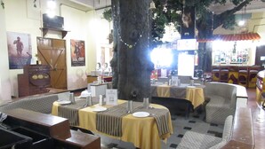 A restaurant with booths, tables, and a large tree in the center. - Ramanashree California Resort (Bengaluru)