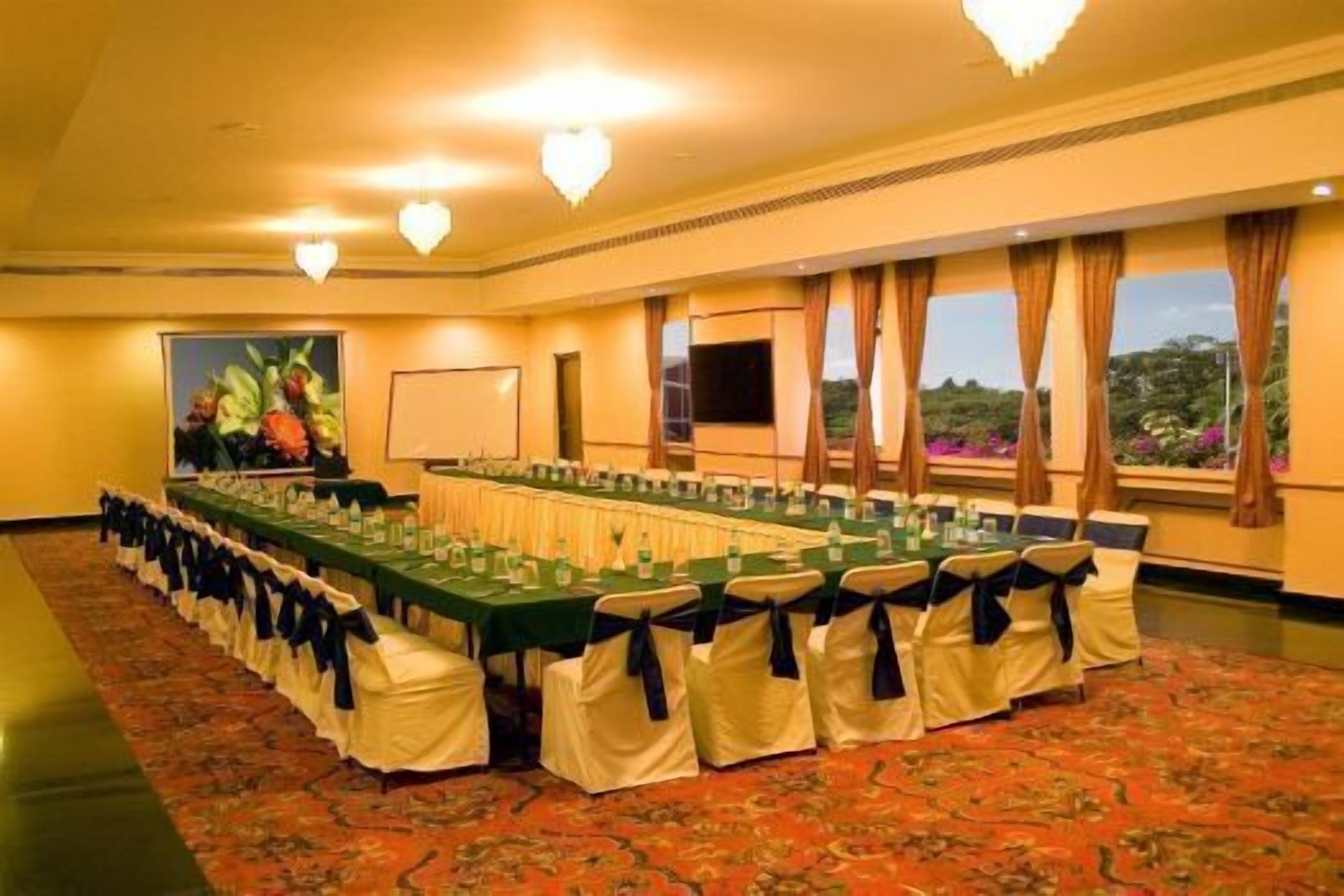 A conference room with a long table, chairs with sashes, a projector screen, and windows with curtains.