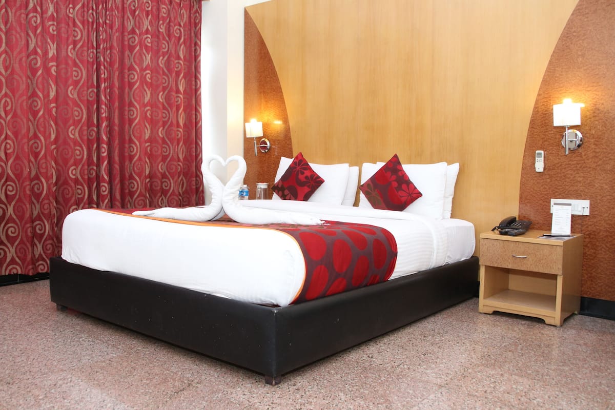Habitación de hotel con una cama grande, dos mesitas de noche, una pared de acento de madera y una cortina roja.