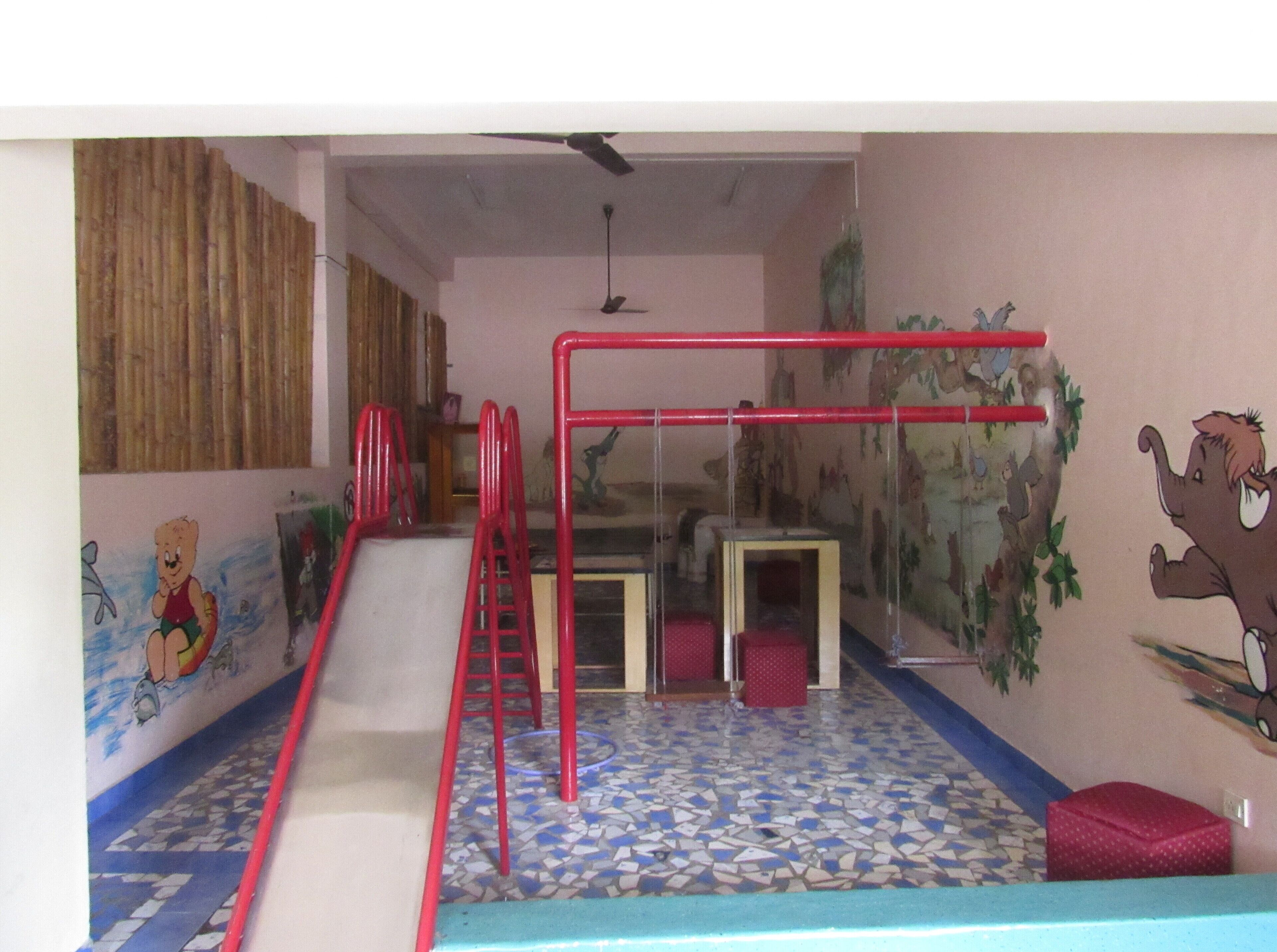 A children's play area with a slide, red climbing structures, and a mural of a bear and elephant.