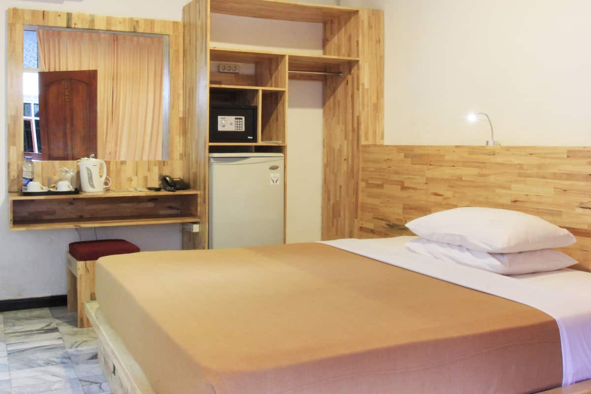 A room with a bed, a wooden wardrobe, a small refrigerator, and a mirror.