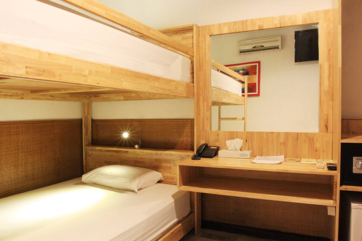 A bunk bed room with a wooden headboard, a bedside lamp, a desk with a telephone, and a mirror.