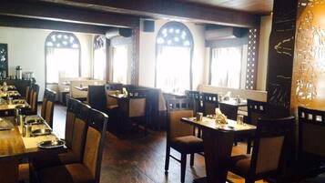 A restaurant with wooden tables and chairs, large windows with decorative frames, and a warm interior ambiance.