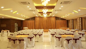 Une salle de banquet avec des rangées de tables et de chaises, une scène avec des rideaux et un lustre.