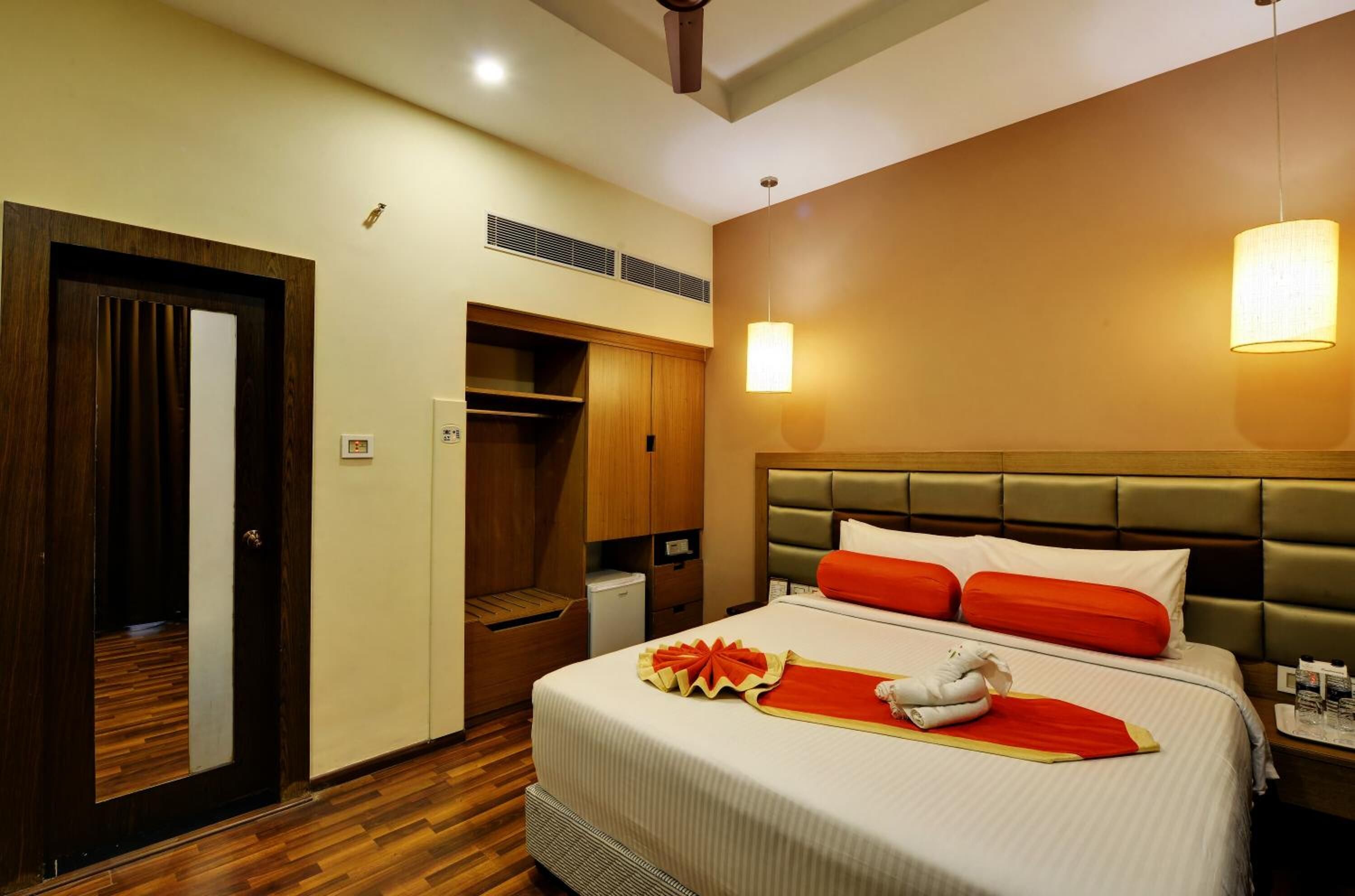A hotel room with a bed, bedside table, lamp, wardrobe, and a small desk.