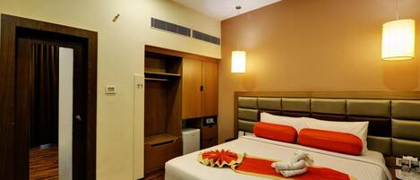 A hotel room with a bed, bedside table, lamp, wardrobe, and a small desk.
