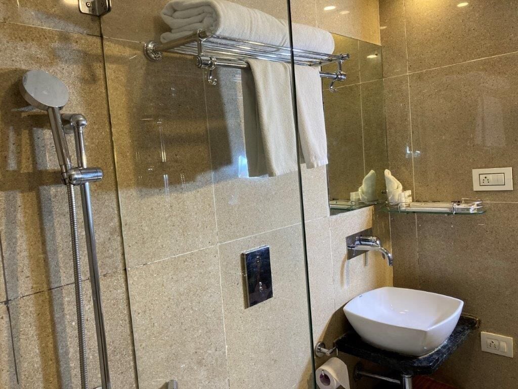 A modern bathroom with a glass-enclosed shower, a white sink, and a towel rack.