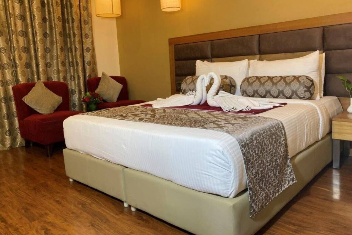 A hotel room with a large bed, a red armchair, a wooden nightstand, and a lamp.