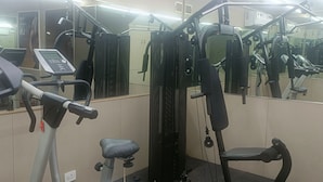 Une salle de sport équipée de matériel d’exercice, notamment un tapis de course, une machine de musculation et un banc.