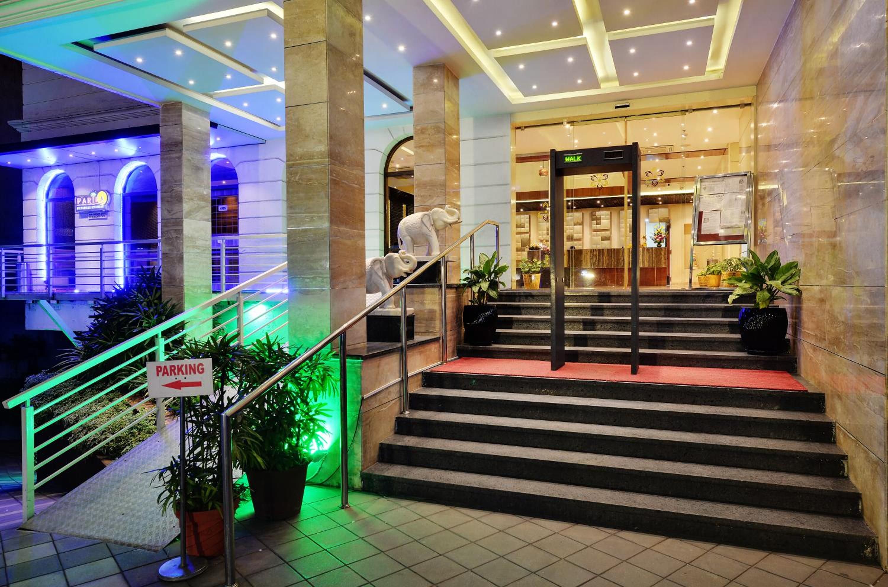 Ein Hotel Eingang mit einer Treppe, die zum Empfangsbereich führt, einem Schild für Parkplätze und einer Rezeption mit einem 'WALK'-Hinweis.