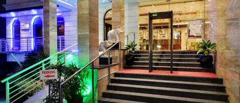 Entrada de hotel con una escalera que lleva al vestíbulo, un cartel que indica el estacionamiento y una zona de recepción con un letrero que dice 'WALK'.