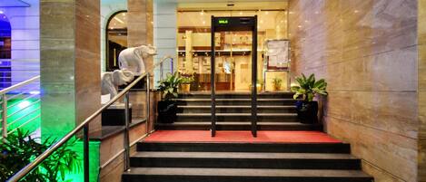 A hotel entrance with a marble staircase, a reception desk, and a sign indicating the direction to the lobby.